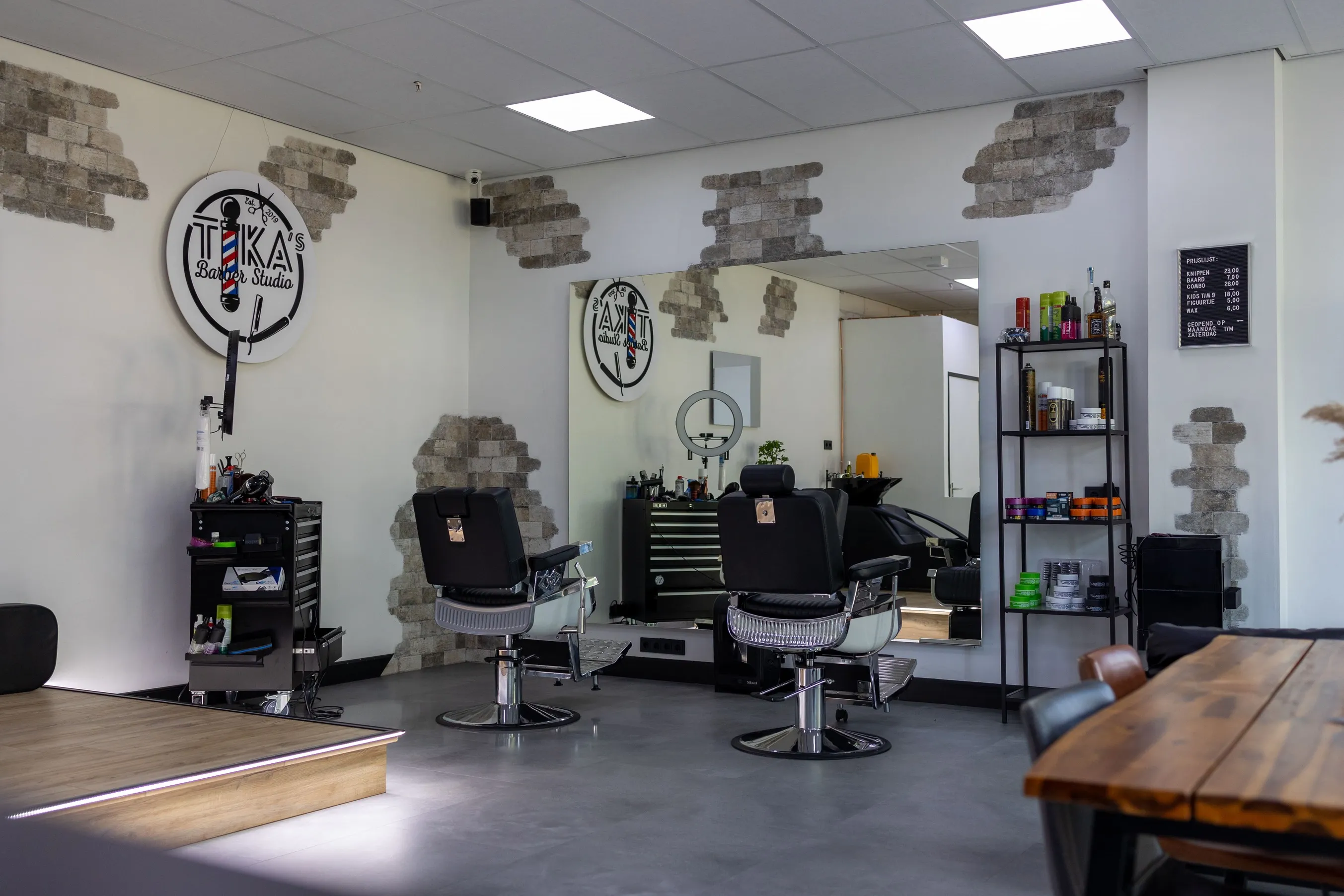 Tika's Barberstudio interieur in Nieuw-Vennep, Haarlemmermeer. Hier zie je een tafel met een vaas en een droge plant. Ook staan er twee kapperstoelen voor een spiegel met daarnaast een rekje.